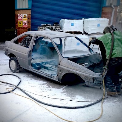 Paint being removed from a car chassis using the soda blasting method